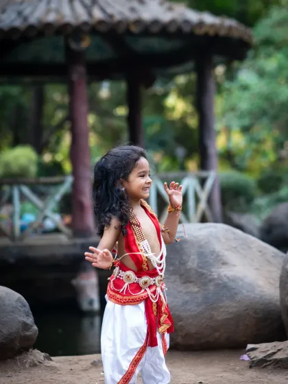 A candid, joyful photo of a boy in a Krishna costume, dancing and playing by the rocks in a park.