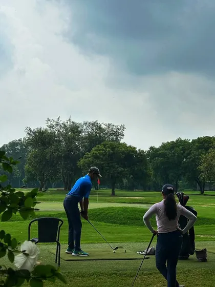 A couple enjoys a practice session together on the range, with the lush course in the background.