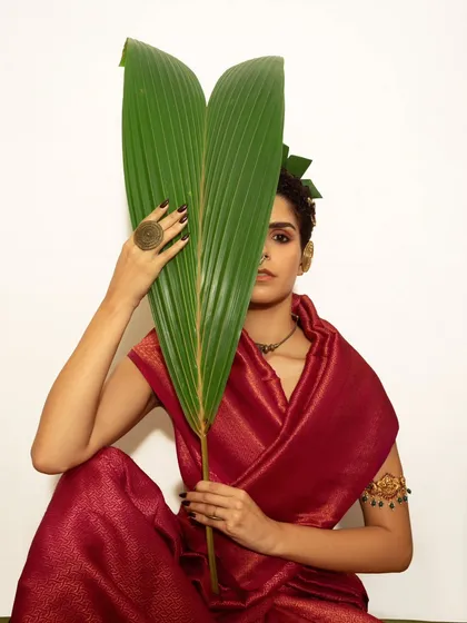 In this shot, the leaf partially obscures the model's face, creating a sense of intrigue and focusing the viewer's attention on her eyes and the textures of the jewelry and fabric.