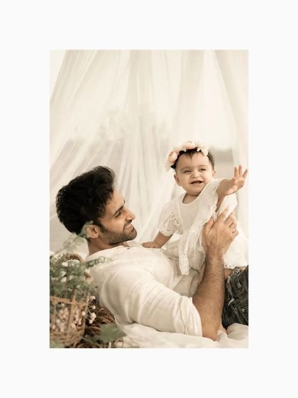 The same father and daughter, now with the baby reaching out with a joyful expression. This photo captures the playful side of their bond, a beautiful memory from a first birthday photoshoot.