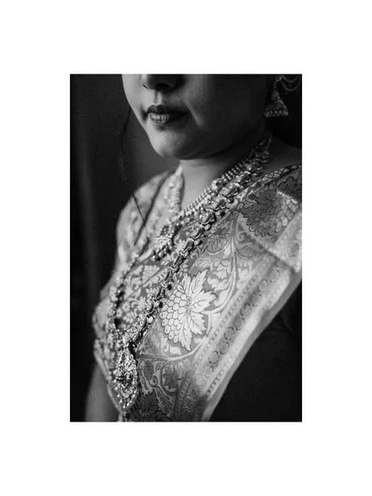 An artistic black and white close-up focusing on the texture of the bride's saree and the detail of her necklace. This shot adds a touch of timeless elegance to the wedding album.