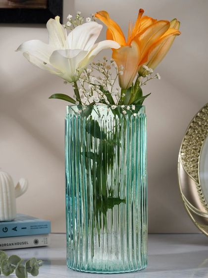 A beautiful turquoise fluted glass vase with lilies. The lighting is carefully controlled to highlight the texture of the glass and the freshness of the flowers.