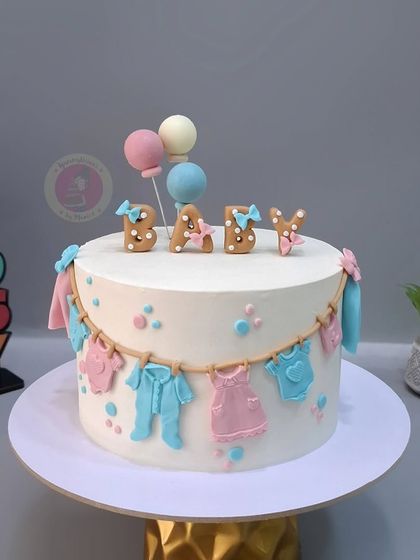 A classic "Boy or Girl" baby shower cake with a clothesline of tiny pink and blue baby clothes.