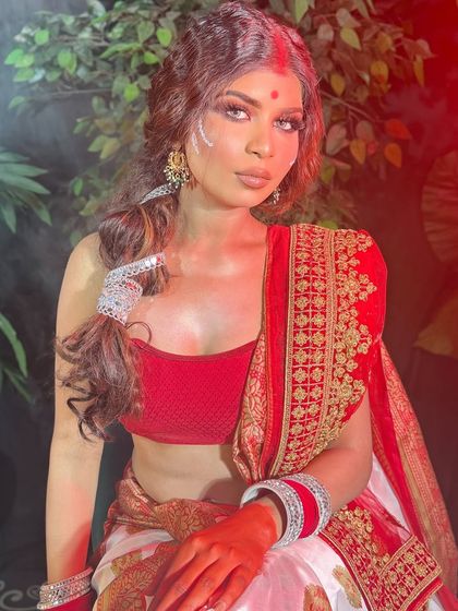 A full view of a Bengali-inspired look, showing the classic red and white saree and crimped, textured hair.
