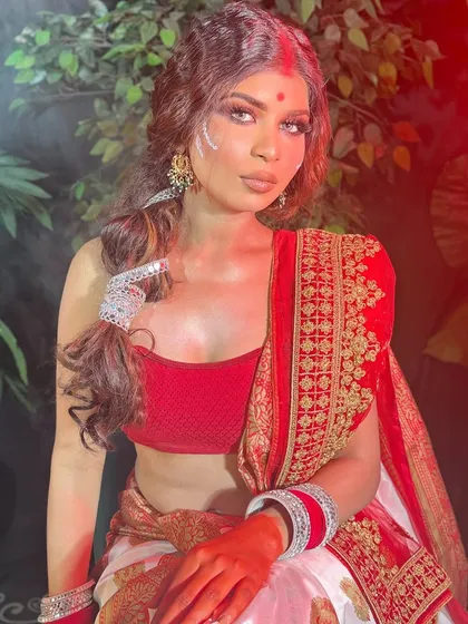 A full view of a Bengali-inspired look, showing the classic red and white saree and crimped, textured hair.