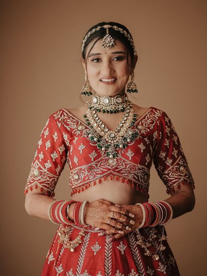 A bright and happy bridal portrait. The bride looks directly at the camera with a warm smile, looking absolutely radiant in her traditional red lehenga and jewelry.