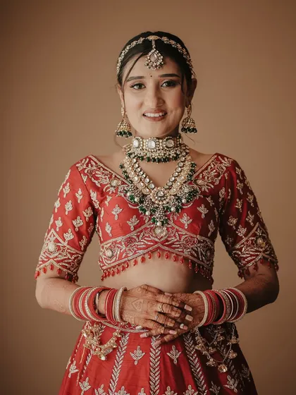 A bright and happy bridal portrait. The bride looks directly at the camera with a warm smile, looking absolutely radiant in her traditional red lehenga and jewelry.