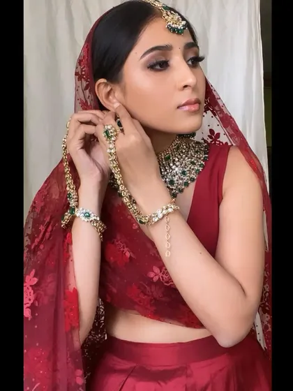 A portrait of the bride in her red and green bridal attire. The makeup is glamorous, with a focus on the eyes.