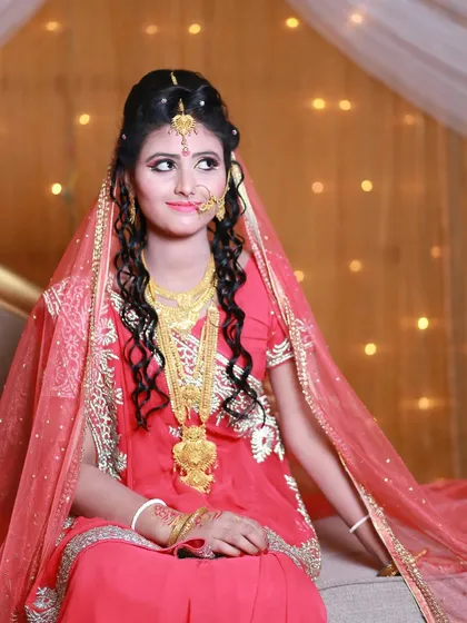 A lovely bridal portrait capturing a candid, thoughtful expression. The soft lighting highlights her intricate gold jewelry and elegant look.