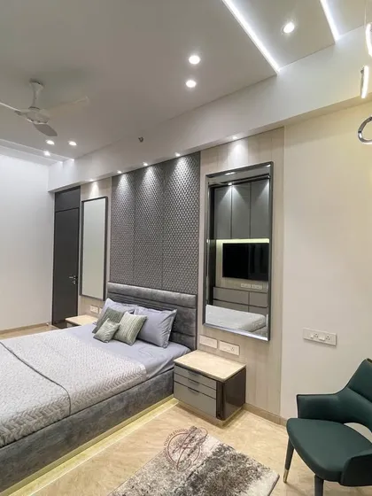 A wide-angle view of the grey bedroom, showing the elegant upholstered bed, integrated wardrobes, and a cozy reading chair. The space is designed to be a grand yet peaceful retreat.