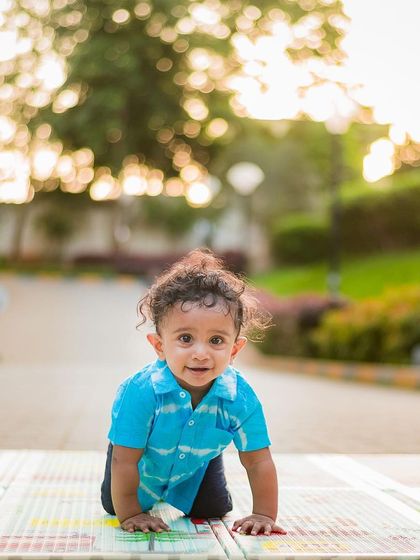 A cute shot of a baby boy crawling on a playmat outdoors, with the golden hour light creating a beautiful bokeh effect in the background.