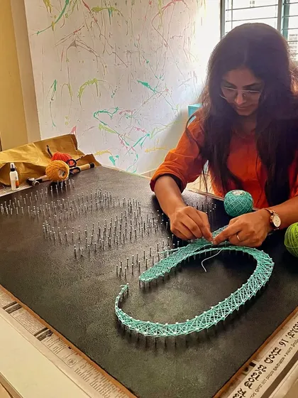 A work-in-progress shot of a large, custom string art nameplate, showing the intricate process of weaving the letters.