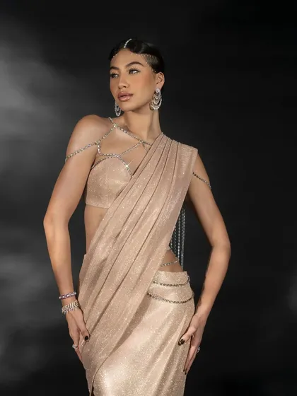 A shot from the 'Gleam Collection' featuring a shimmering beige saree. The lighting is designed to catch the metallic texture of the fabric and the sparkle of the body jewelry.