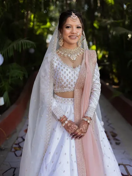 A full-length shot of a bride looking radiant in her white lehenga. The polki necklace and soft pink dupatta create a look that is both romantic and timeless.