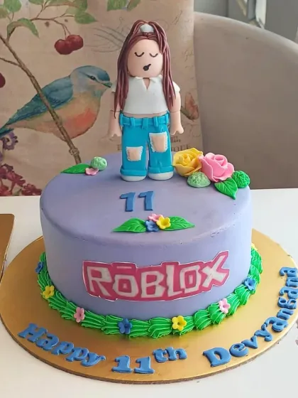 A personalized Roblox cake for an 11th birthday, featuring a custom avatar figure and the iconic game logo on a purple base.