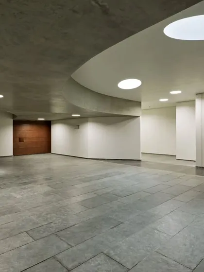 The main gallery space at Vismaya is characterized by its clean lines, sweeping curves, and the soft, diffuse light from circular skylights. The architecture provides a serene and neutral environment for the display of art.