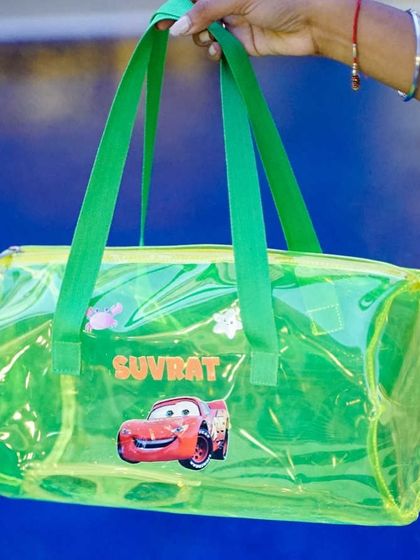 A neon green jelly duffle bag personalized for a young fan of the movie 'Cars'. It features the name 'Suvrat' and a Lightning McQueen patch, perfect for a themed birthday party.