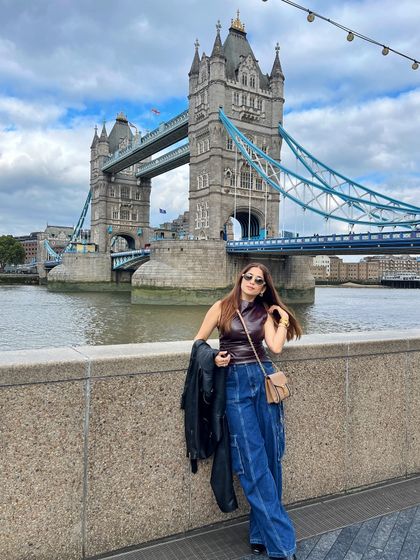 A photo from my London camera roll, standing in front of the iconic Tower Bridge. I'm wearing a leather top with denim cargo pants, a perfect example of my street style vibe.