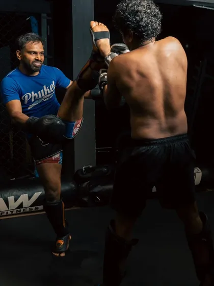 A coach holds a pad to catch a high kick, demonstrating the trust and technique involved in partner drills.