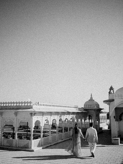 A black and white shot of the couple walking hand-in-hand through a sun-drenched courtyard. The grainy texture and classic composition give it a timeless, film-like quality.