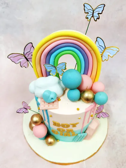 An angled view of the gender reveal cake, highlighting the vibrant rainbow topper and delicate butterfly details.