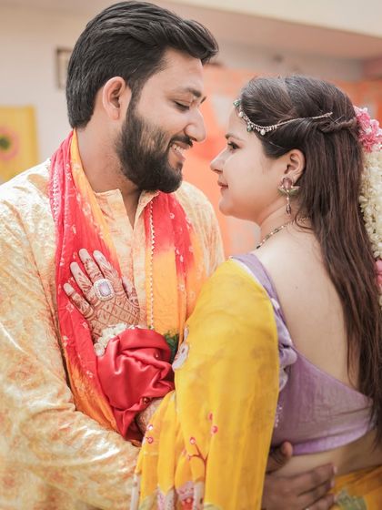 A romantic portrait of a couple during their haldi, sharing a look, with the bride's mehendi-adorned hand on the groom.