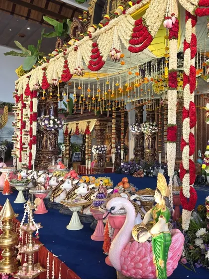 A grand and colorful temple-style mandapam, with a Hanuman statue and intricate floral pillars.