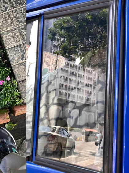 The city reflected in the window of a blue bus, a fleeting, distorted view of the architecture outside.