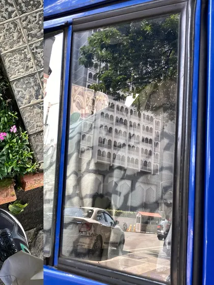 The city reflected in the window of a blue bus, a fleeting, distorted view of the architecture outside.
