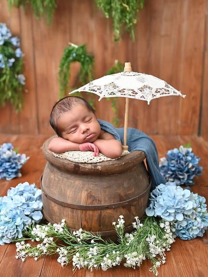 A dreamy floral setup. This newborn sleeps peacefully under a delicate lace umbrella, surrounded by beautiful blue hydrangeas.