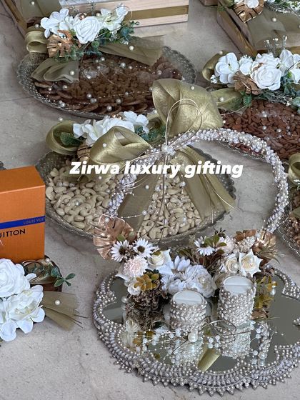 A stunning display of wedding trousseau trays. These platters are filled with dry fruits and gifts, including a Louis Vuitton box, all decorated in a sophisticated gold and white theme.