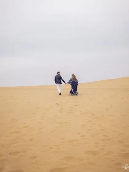 Priyangi and Kishan walk across the vast sand dunes of Jaisalmer. This epic, wide shot captures a sense of adventure and the beginning of their journey together.