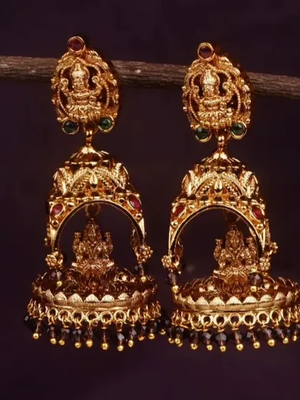 These traditional jhumkis feature a matte gold finish and are adorned with a Goddess Lakshmi motif. This pair has black bead drops for a classic and striking look.