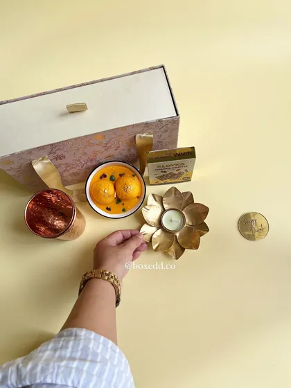 Preparing a Diwali hamper that includes traditional sweets like motichoor laddoos, paired with a copper tumbler and a decorative diya.