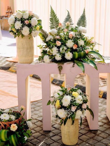 Decor details featuring modern arched stands and bamboo vases filled with fresh white chrysanthemums and ferns.