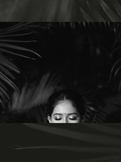 An artistic and moody black and white portrait of the bride, with her face partially framed by palm leaves, creating a sense of mystery and beauty.
