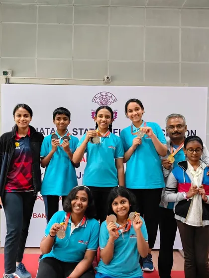 A group of our state-level medalists posing with their coaches. This picture captures the strong bond and shared success within our shooting family.