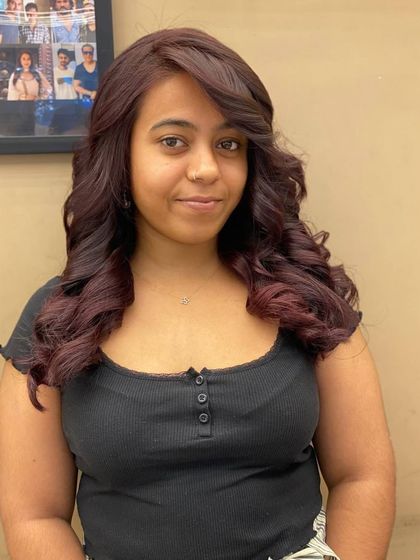 A smiling client showing off her new, rich red hair color. The voluminous curls and deep tone create a look that is both glamorous and full of confidence.
