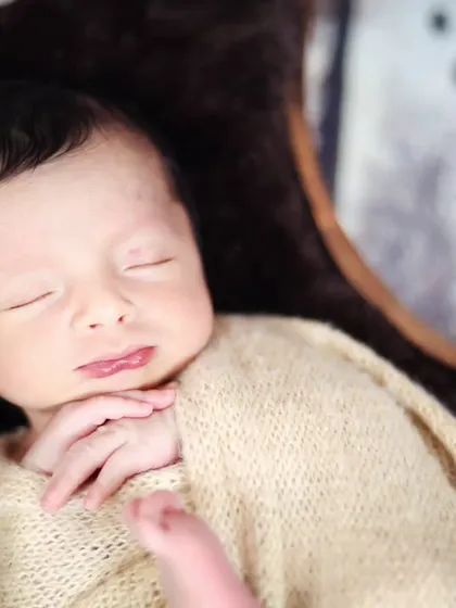 A close-up shot of the newborn in the wooden moon bowl, capturing their serene expression and tiny hands.