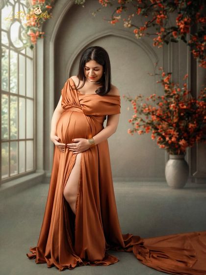 A full-length portrait showing the beautiful drape of this bronze maternity gown. The studio setting with florals adds a touch of romance.