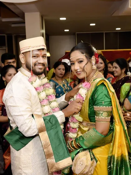 The bride and groom during the garland exchange. Her yellow and green Nauvari look is a classic choice, and the makeup is designed to complement these vibrant colors.