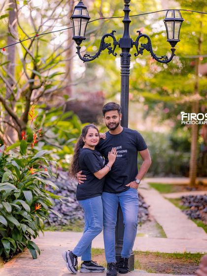 A casual and stylish couple poses by a classic lamppost on a garden pathway.