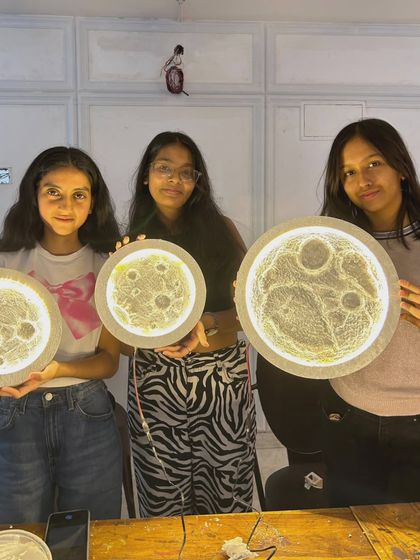 Three students proudly display their finished 3-D moon lamps. Each piece has its own unique texture and character, making it a special piece of home decor.
