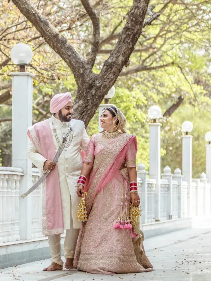 A beautiful portrait of a Sikh couple on their wedding day, standing together in a serene outdoor setting with elegant white pillars.