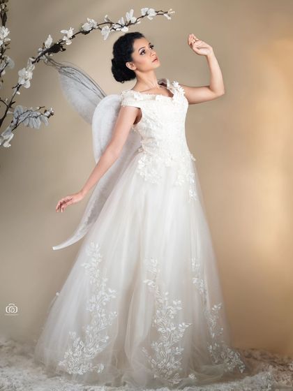 A full-length shot of the model in a white gown with fairy wings. The soft, warm lighting and the ethereal props create a beautiful and enchanting scene.