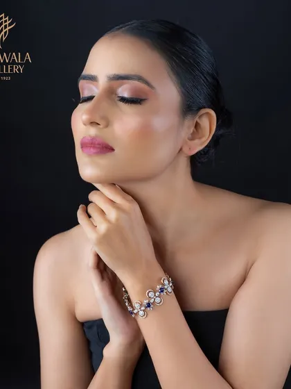 A model wears a beautiful floral bracelet with blue sapphires, pearls, and diamonds, perfect for festive occasions.