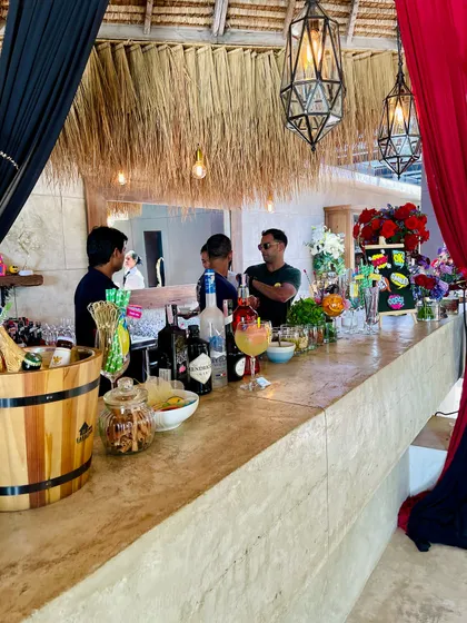 A rustic-themed bar setup for a daytime event, featuring a thatched roof and natural wood counter. We work with you or your event planner to ensure our bar design complements the overall decor and vibe.