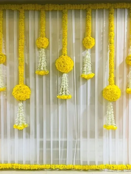 A classic and elegant decor choice for Ganpati or any home puja, featuring bright yellow drapes and traditional floral hangings.