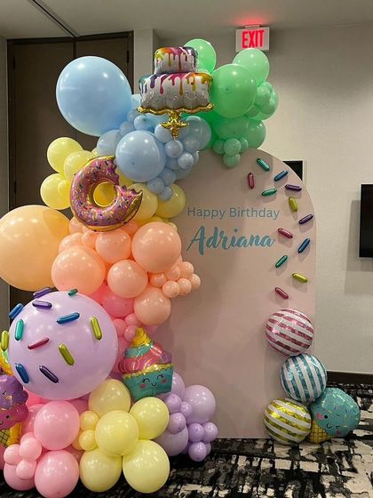 A delicious-looking candy and donut themed birthday party. This setup features a pastel balloon arch decorated with giant donut, cupcake, and ice cream cone balloons.