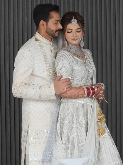A stunning full-length photo of the couple. The bride's soft, minimal makeup perfectly complemented her intricate white lehenga.